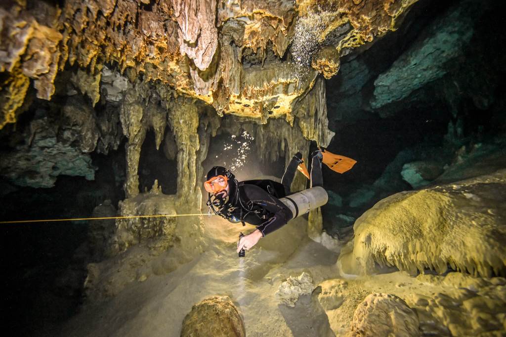 Scuba diver in sidemount gear and an orange mask and fins inside a submerged cavern