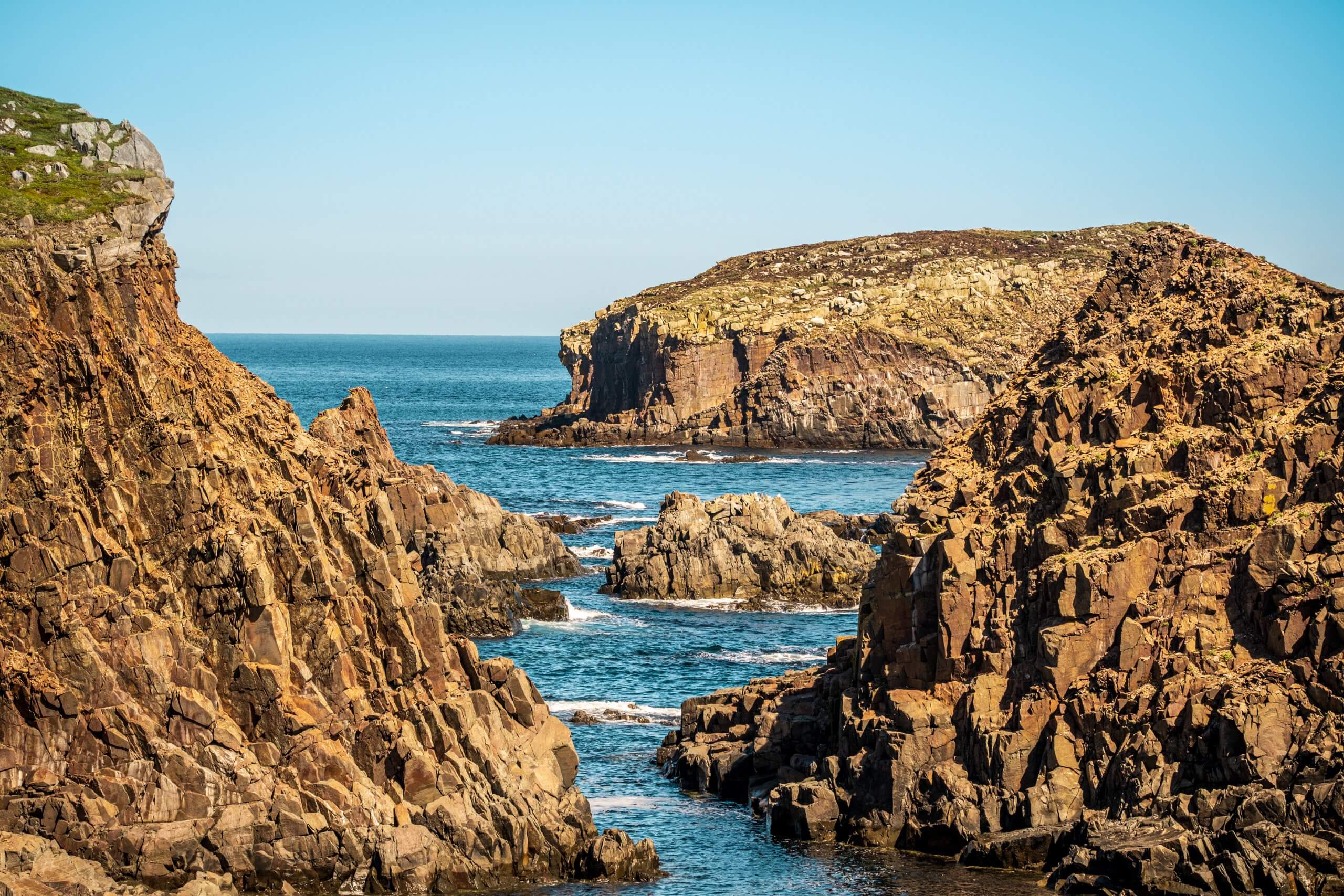 The blue sea appears through cracks in the rocky cliffs at Elliston, Newfoundland