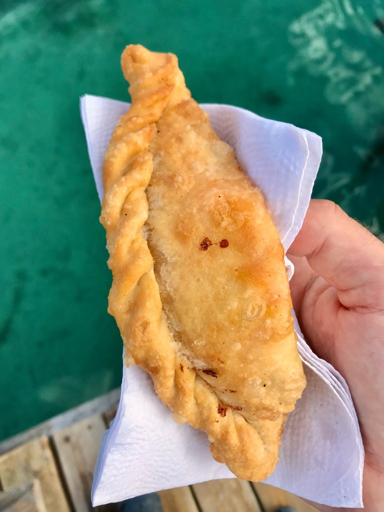 A pastelito held in a hand with a napkin over a dock at the sea