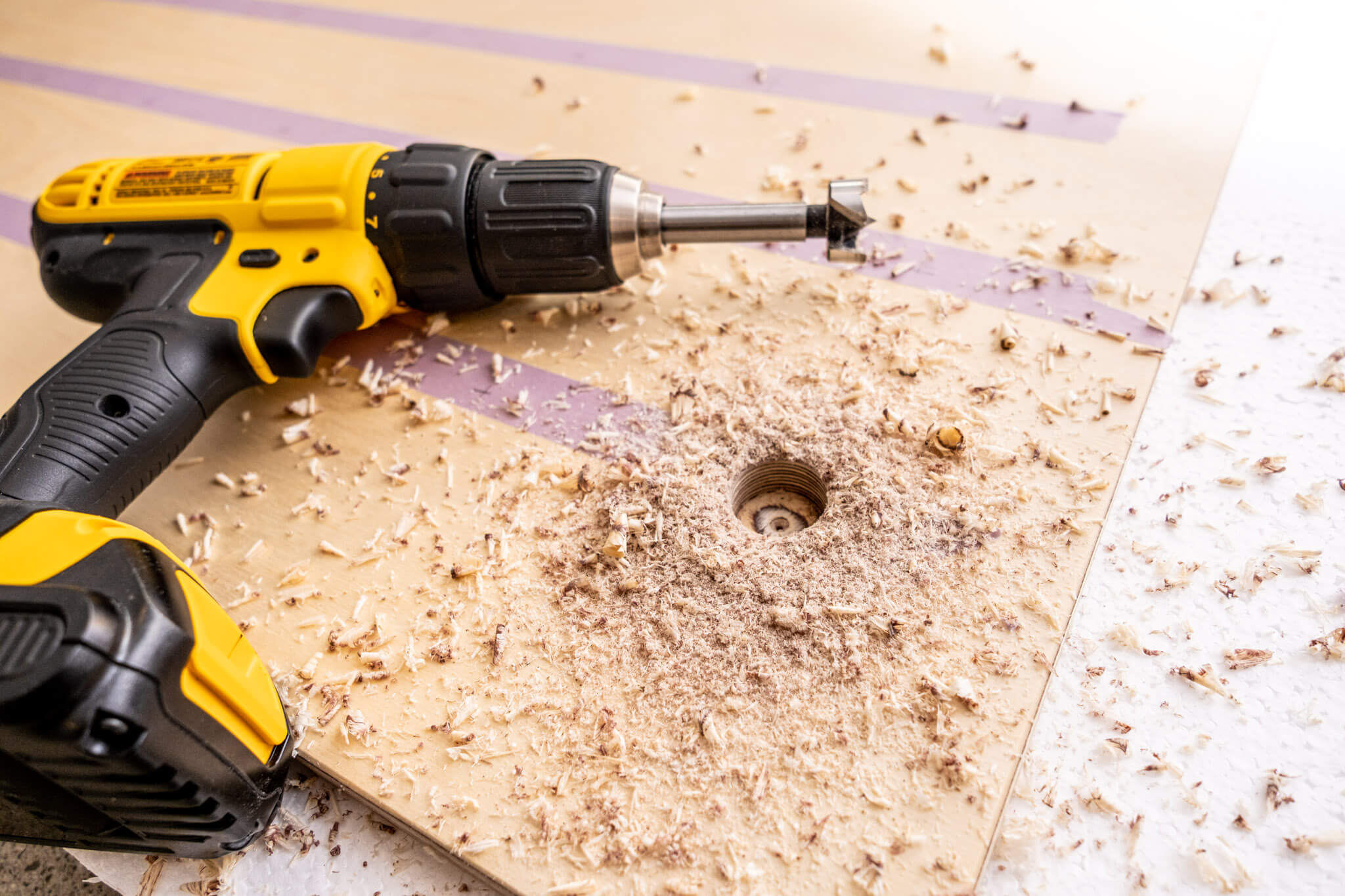A cordless drill with a Forstner bit cutting holes in Baltic birch plywood