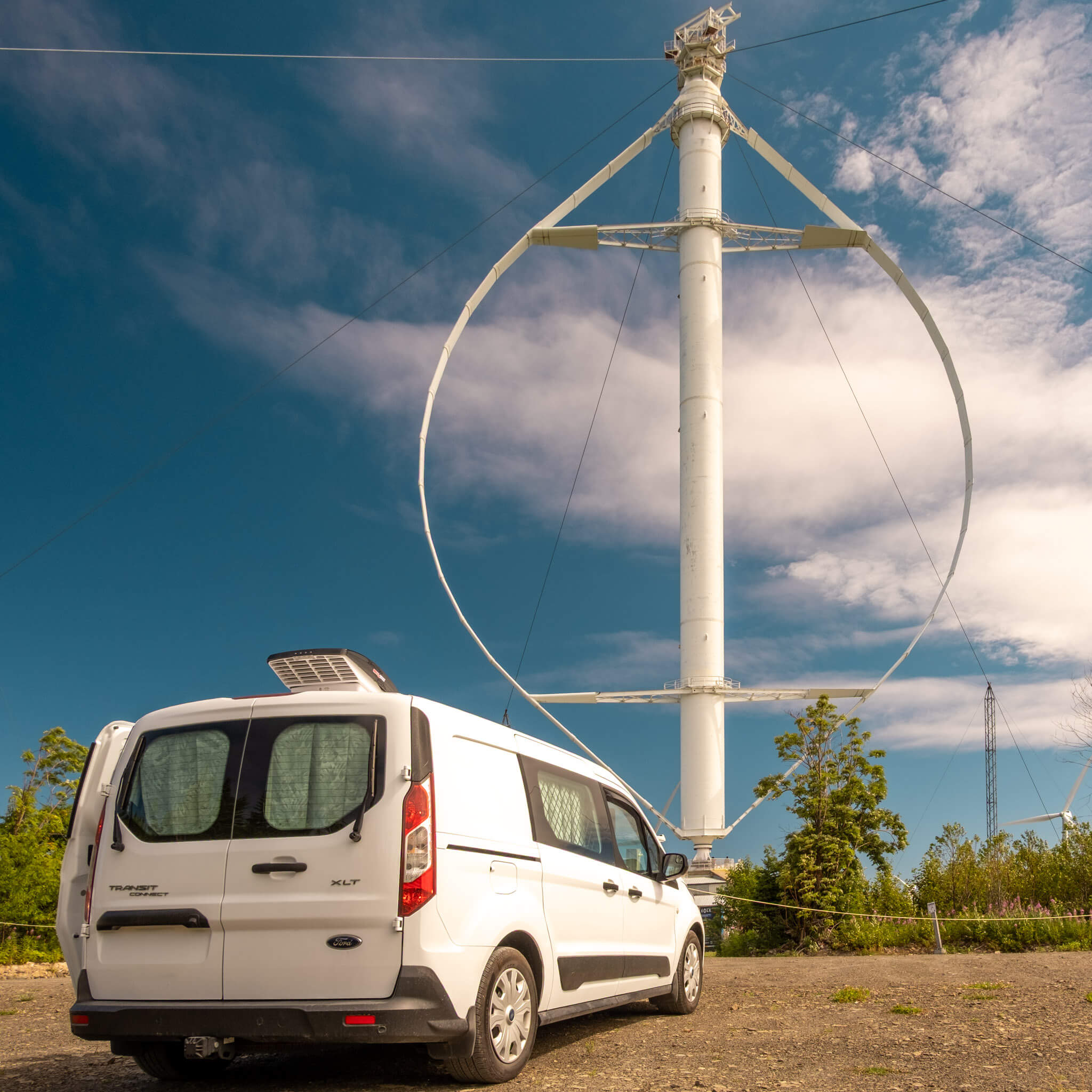 Transit Connect camper van in front of the Projet Éole vertical-axis wind turbine in Cap-Chat, Quebec